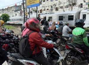 Pengendara motor menunggu di perlintasan sebidang saat kereta melintas di Bekasi Timur