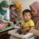 Ibu dan anak mengikuti penimbangan di posyandu untuk pencegahan stunting di Indonesia