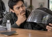 Pengendara memeriksa baret pada visor helm sebelum melakukan perawatan atau pemolesan.